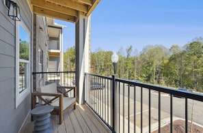 A wooden deck with a table and chairs, a street view with cars, and a forest in the background. - Landing Stylish 1bd, Clubhouse, Gym (Raleigh)