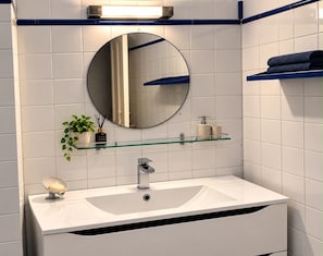 A modern bathroom with a white sink, a round mirror, and a glass shelf with toiletries. - aroma house (Tulle)