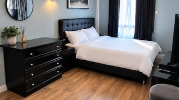 A hotel room with a bed, a black dresser, a round mirror, a wall-mounted light, and a painting.