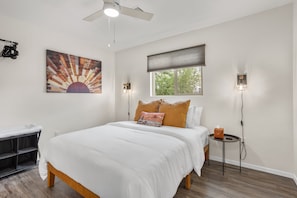 Une chambre à coucher comprenant un lit, un bureau, une chaise, une fenêtre avec des stores et un ventilateur de plafond.