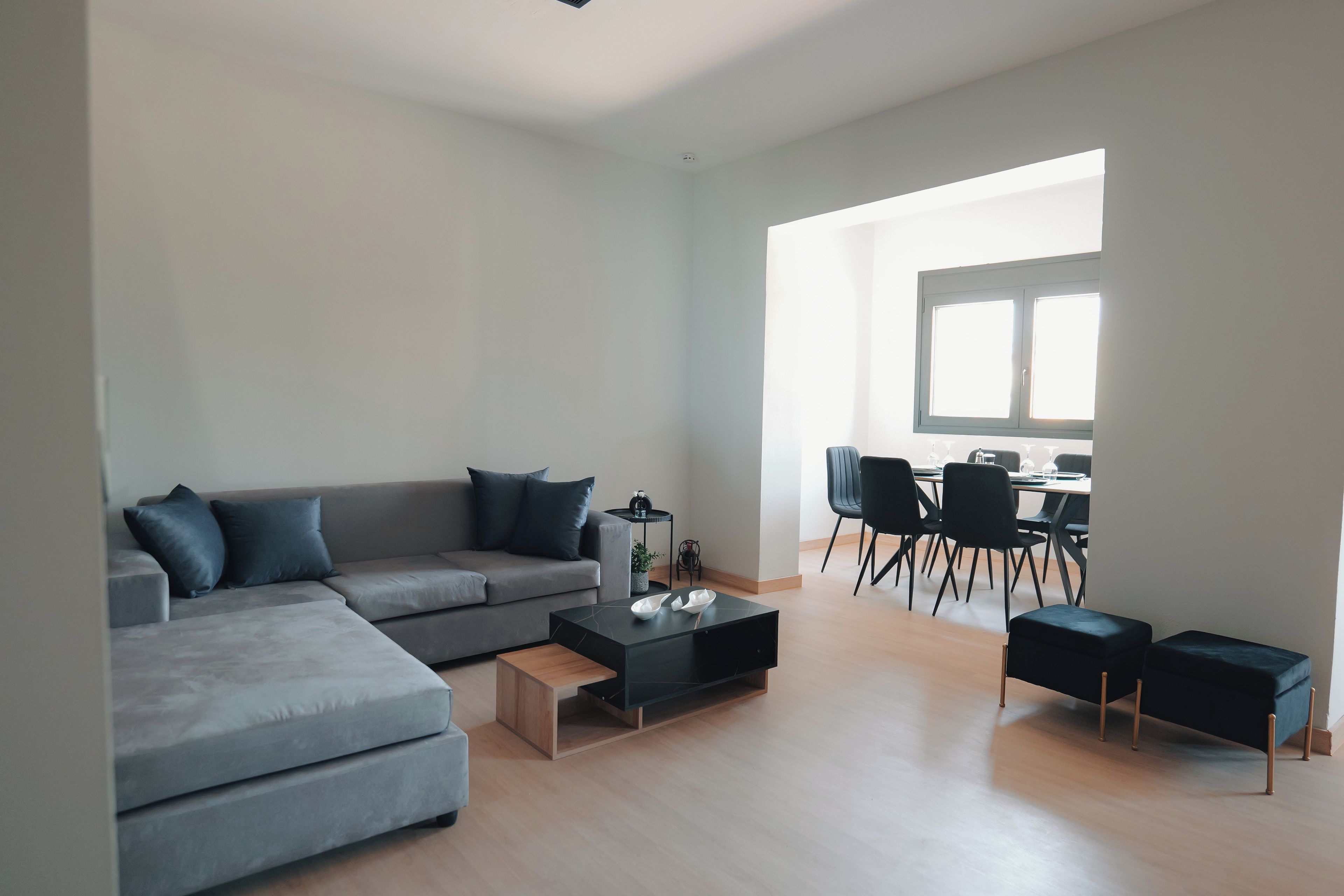 A modern living room with a grey sectional sofa, a coffee table, and a dining area with a table and chairs.