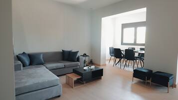 A modern living room with a grey sectional sofa, a coffee table, and a dining area with a table and chairs.
