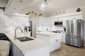 A modern kitchen with white cabinetry, stainless steel appliances, and a herringbone wood floor. - FreePoolHeat|HotTub|Sleeps18|Arcade|ThemeRooms (Mesa)