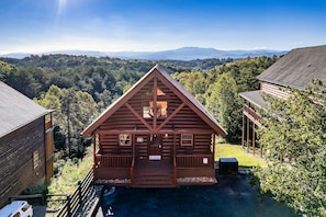 A wooden cabin with a porch, surrounded by a forest and mountains in the background. - Mountain Views, 2 King Suites, Hot Tub, Cabin with AC in peaceful Sevierville (Sevierville)