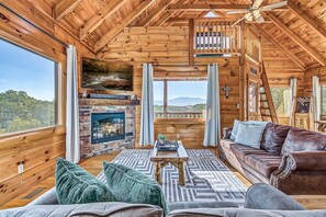 A log cabin interior with a fireplace, a sofa, a coffee table, and a television. - Mountain Views, 2 King Suites, Hot Tub, Cabin with AC in peaceful Sevierville (Sevierville)