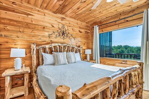 A wooden cabin bedroom with a bed, nightstands, and a window with a view. - Mountain Views, 2 King Suites, Hot Tub, Cabin with AC in peaceful Sevierville (Sevierville)