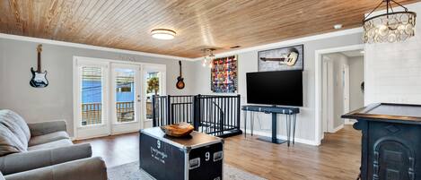 A spacious living room with a high ceiling, a large TV, and a collection of guitars on the wall.