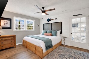A bedroom with a wooden bed, a ceiling fan, a guitar, a wall-mounted clock, and a door with a sign. - Music Themed Retreat with Private Heated Pool (Tybee Island)