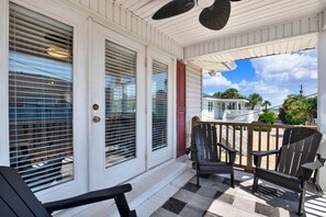 A covered porch with two Adirondack chairs, a checkered floor, and a view of a white house with a red door. - Music Themed Retreat with Private Heated Pool (Tybee Island)