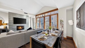 A modern living room with a fireplace, a large TV, and a dining area set for a meal. - The Iron Horse by Avantstay Mountain Views Pool & Spa Walk to Gondola Skating Rink & Shops (Truckee)