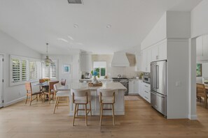A modern kitchen with white cabinetry, a central island with bar stools, and stainless steel appliances. -  Beautifully remodeled 3-bedroom home  located close to the beach in Cardiff, CA (Encinitas)