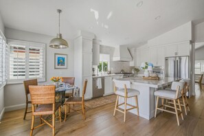 A modern kitchen with white cabinetry, a central island, and a dining area with wicker chairs. -  Beautifully remodeled 3-bedroom home  located close to the beach in Cardiff, CA (Encinitas)
