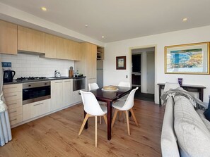 A modern kitchen with wooden cabinets, a dining table with chairs, and a sofa in a living area. - Private Genuine Lakefront Suite, Queenstown (Queenstown)