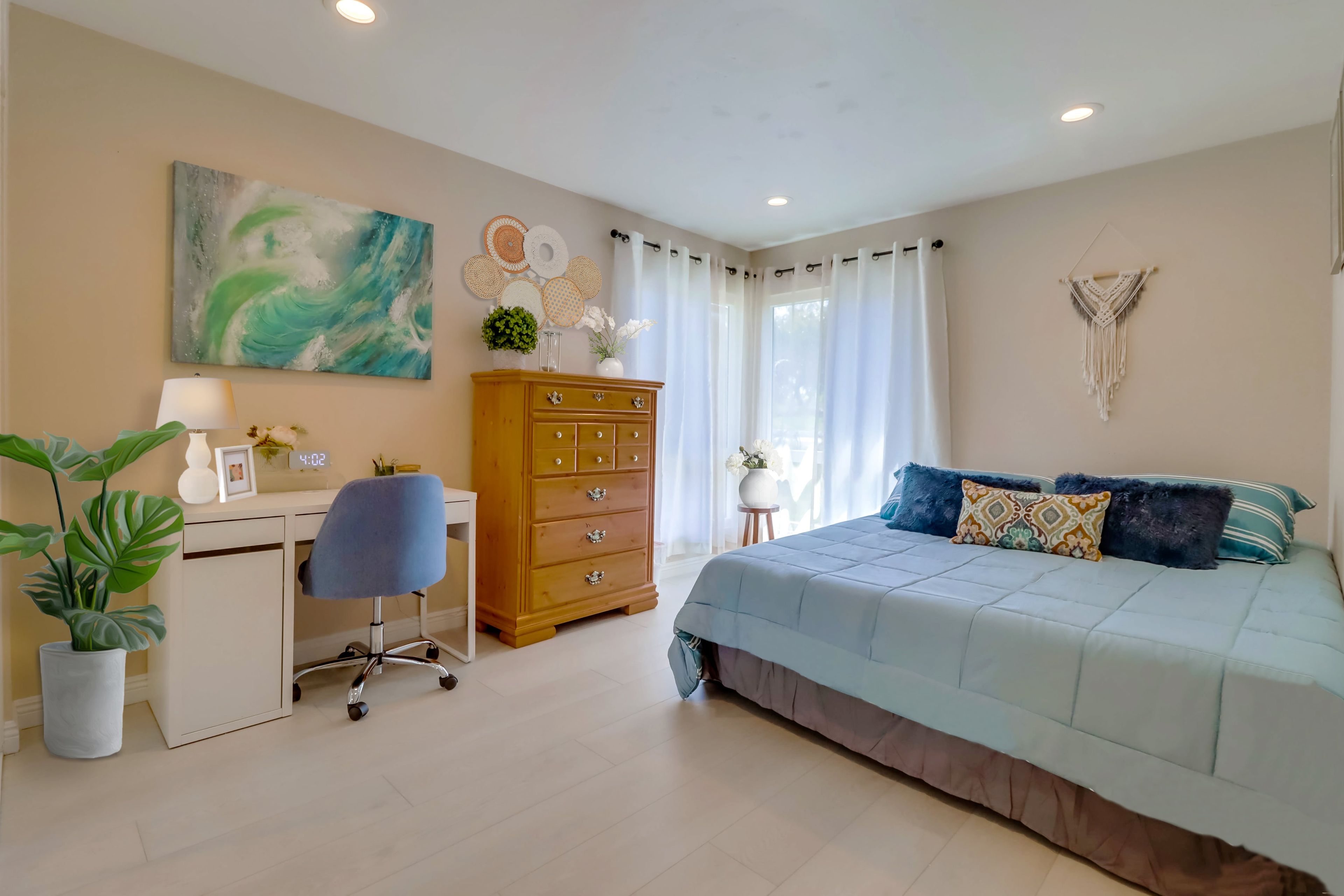 Un dormitorio con cama, escritorio, silla, cómoda y una pared decorada.