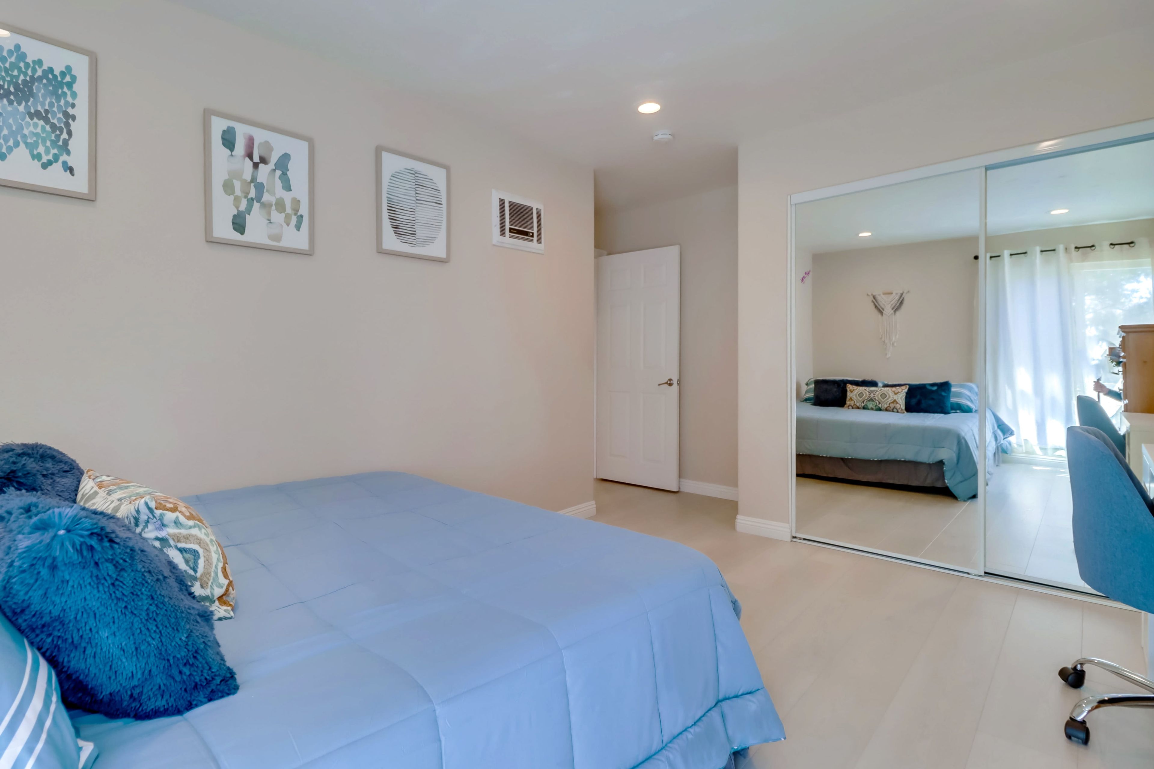 A bedroom with a bed, a mirror, and a door leading to another room.