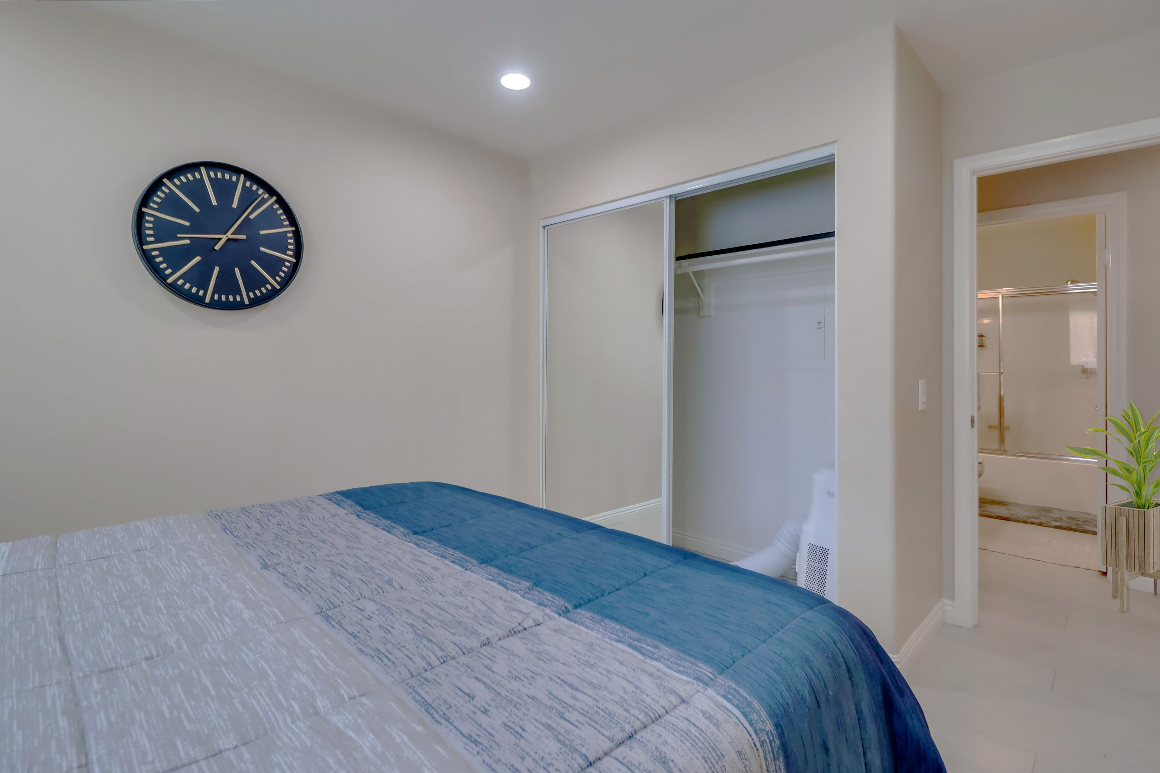 A bedroom with a bed, a wall clock, a closet, and a bathroom visible through an open door.