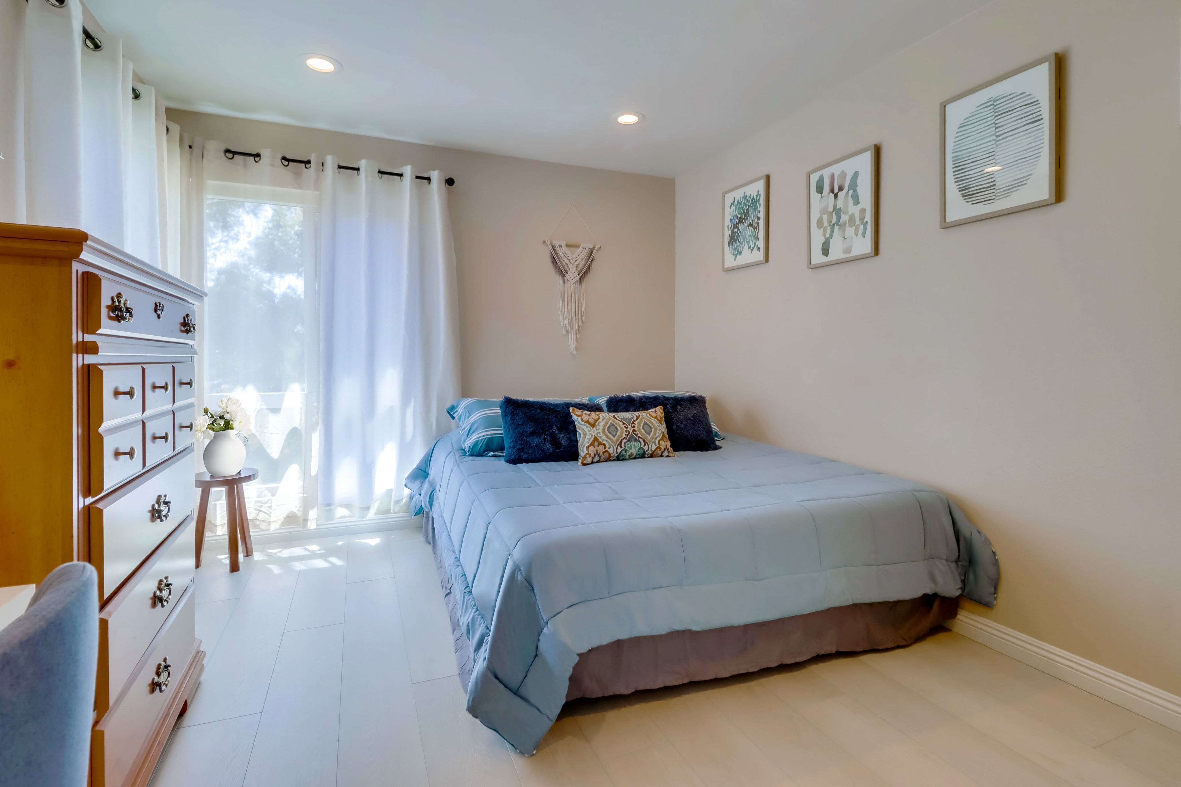 Een slaapkamer met een bed, een kaptafel, een dressoir en een raam met gordijnen.