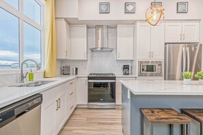 A modern kitchen with white cabinetry, stainless steel appliances, a built-in oven, and a large island with bar stools. - ~XtraLargePrivateFencedYard|BBQ|AC|2FamilyRooms (Calgary)