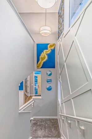 A modern interior with a staircase, a wall-mounted light fixture, and a large abstract painting. - ~XtraLargePrivateFencedYard|BBQ|AC|2FamilyRooms (Calgary)