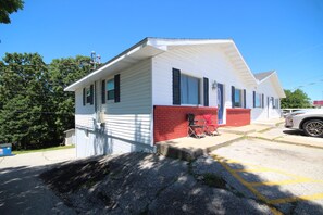 A single-story building with a white and red facade, a small porch with two chairs, and a parking lot with a yellow line.