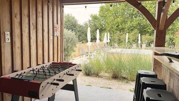 Un espace extérieur avec piscine, une table de baby-foot, des chaises longues et une terrasse en bois.