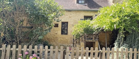 A stone building with a wooden fence, a flower pot, and a tree.