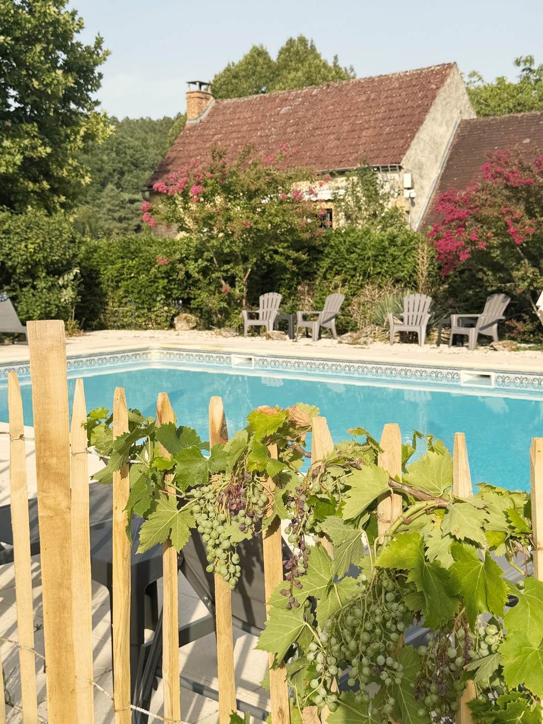 A poolside area with a wooden fence, a row of chairs, and a building with a red roof in the background.