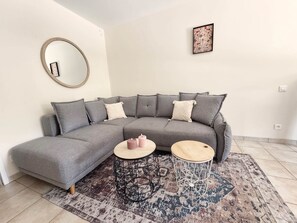 A modern living room with a grey sectional sofa, two round side tables, a patterned rug, a round mirror, and a framed picture on the wall. - La Violette – Spacious holiday home with private terrace and views (Meyrals)