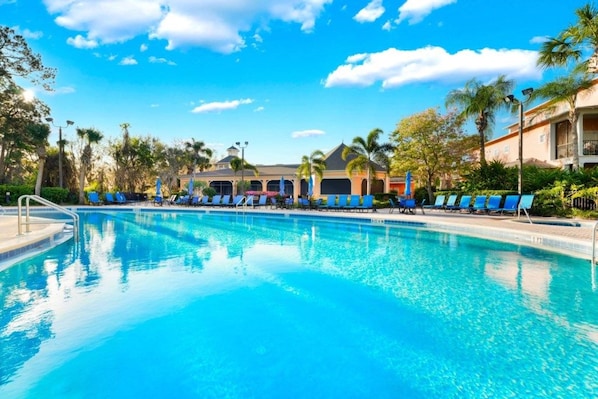Una piscina azul cristalina con sillas de descanso y palmeras.