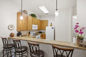 A modern kitchen with wooden cabinets, a central island with bar stools, a microwave, a stove, and a refrigerator. - 2BR Bahama Bay Condo Near Disney (Davenport)