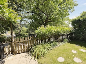 Ein Garten mit Holzzaun, Rasen mit trittfesten Steinen und verschiedenen Pflanzen.
