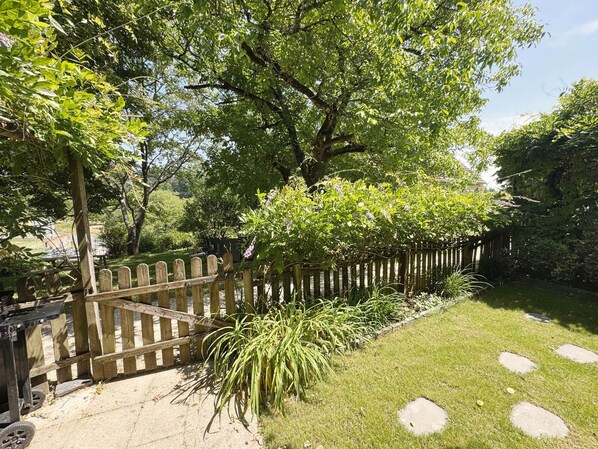 Un jardín con valla de madera, césped con losetas y diversas plantas.