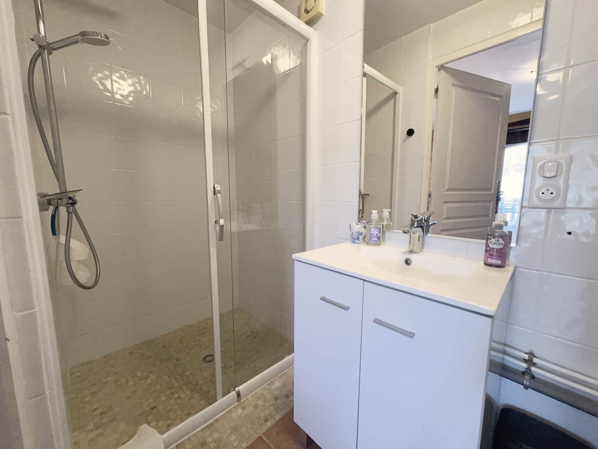 Un baño con cabina de ducha de vidrio, un lavamanos blanco con espejo y un armario.