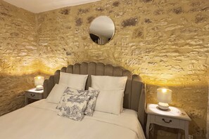Un dormitorio con pared de piedra, un espejo redondo, una cama con dos almohadas y lámparas de noche.