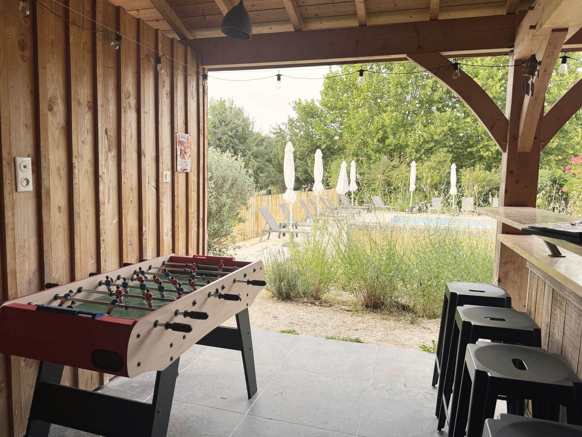 An outdoor pool area with a foosball table, lounge chairs, and a wooden deck.