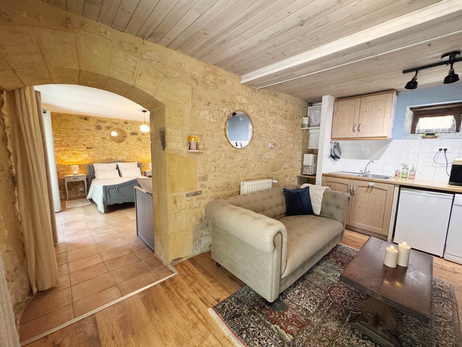 A cozy interior with a stone wall, a sofa, a small rug, and a kitchen area.