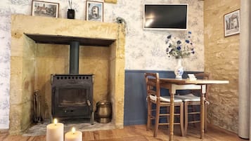 A rustic room with a stone fireplace, a table with chairs, and a flat-screen TV mounted on the wall.