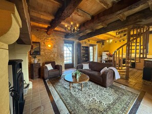 A rustic interior with a fireplace, a sofa, a coffee table, and a staircase. - Le Bleuet – Holiday cottage for 4 people (Meyrals)