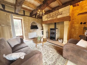 A rustic living room with stone walls, a fireplace, and wooden furniture. - Le Bleuet – Holiday cottage for 4 people (Meyrals)