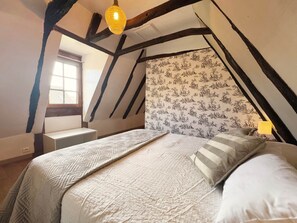 A bedroom with a bed, a nightstand, a window, and a hanging light fixture. - Le Bleuet – Holiday cottage for 4 people (Meyrals)