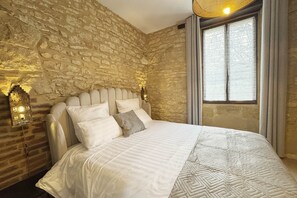 A room with a stone wall, a bed with white bedding, and a window with curtains. - La Campanule – Spacious holiday home for 6 people with private hot tub (Meyrals)