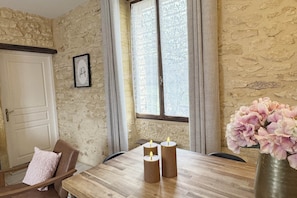 Een eetruimte met een houten tafel, drie kaarsen, een vaas met bloemen en een stenen muur.