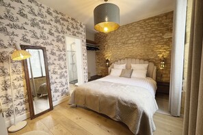 Een slaapkamer met een stenen muur, een bed met een beddekleed met dessin, een hanglamp en een spiegel.