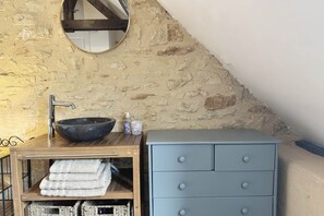 Een badkamer met een stenen muur, een ronde spiegel, een houten wastafelmeubel met een wastafel en een blauwe kast.