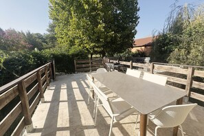 Ein Essbereich im Freien mit Tisch und Stühlen, umgeben von einem Holzzaun und Bäumen.