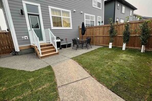 A residential backyard with a patio, a wooden staircase, a barbecue grill, and a fenced area with potted plants. - ~PrivateFencedYard | 2FamilyRms | SunshineYellow (Calgary)