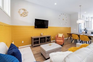 A modern living room with a sofa, ottoman, and a television mounted on the wall. - ~PrivateFencedYard | 2FamilyRms | SunshineYellow (Calgary)