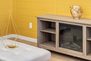 A room with a wooden entertainment center, a white cushioned bench, and a decorative glass vase on top. - ~PrivateFencedYard | 2FamilyRms | SunshineYellow (Calgary)