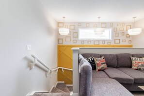 A modern living room with a grey sofa, patterned cushions, and a yellow accent wall. - ~PrivateFencedYard | 2FamilyRms | SunshineYellow (Calgary)
