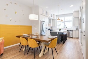 A modern kitchen with a central island, white cabinetry, and a yellow accent wall. - ~PrivateFencedYard | 2FamilyRms | SunshineYellow (Calgary)